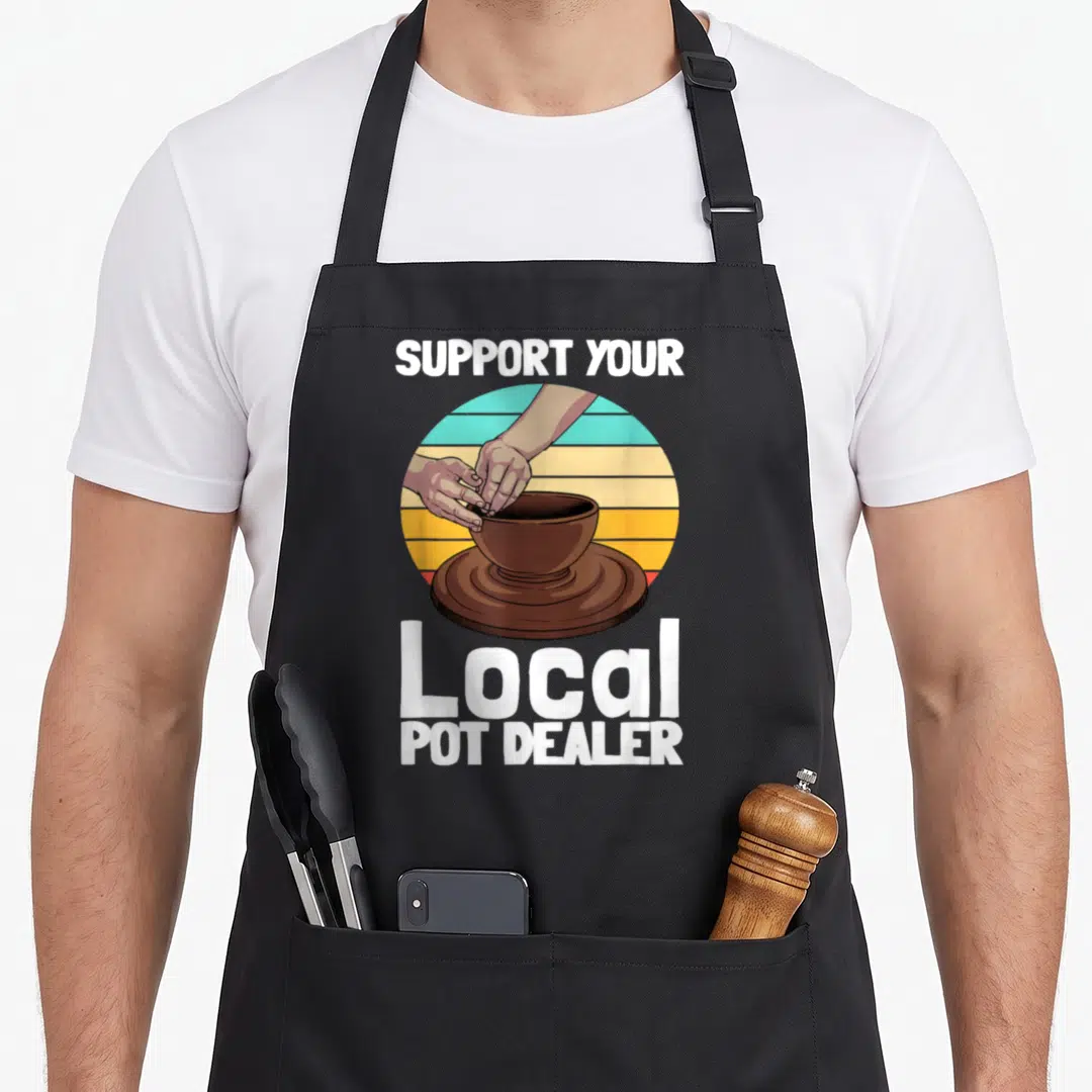 Pottery dealer apron - Retro sunset circle with hands shaping brown pot on wheel, white text reads Support Your Local — shown on a black cotton canvas apron against a white background