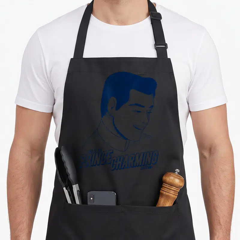 Cinderella prince charming apron - Blue cartoon man portrait with text THIS IS MY PRINCE CHARMING COSTUME below — shown on a black cotton canvas apron against a white background