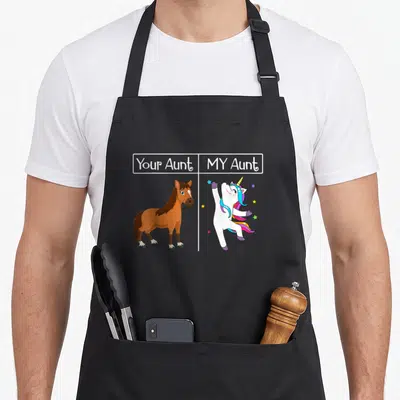 Auntie unicorn apron - Your Aunt MY Aunt text above brown horse and white unicorn with stars — shown on a black cotton canvas apron against a white background