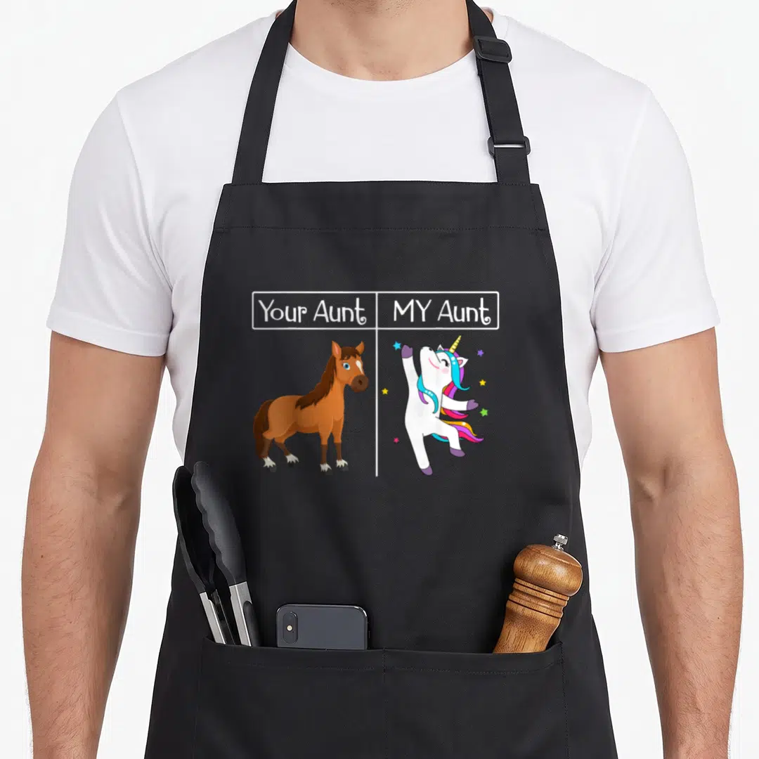 Auntie unicorn apron - Your Aunt MY Aunt text above brown horse and white unicorn with stars — shown on a black cotton canvas apron against a white background
