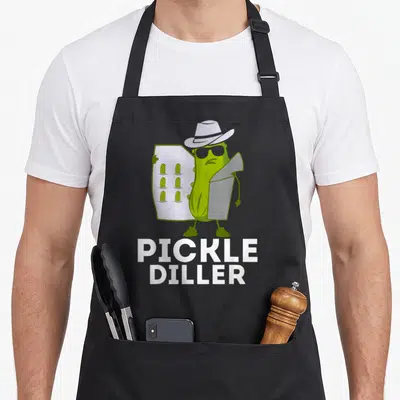 Diller pickle apron - Green cartoon pickle in hat and sunglasses holding a menu with small pickle drawings and white — shown on a black cotton canvas apron against a white background