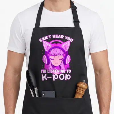 Hear girls korean apron - Cartoon girl with pink cat ears and headphones surrounded by white text about K-pop listening — shown on a black cotton canvas apron against a white background