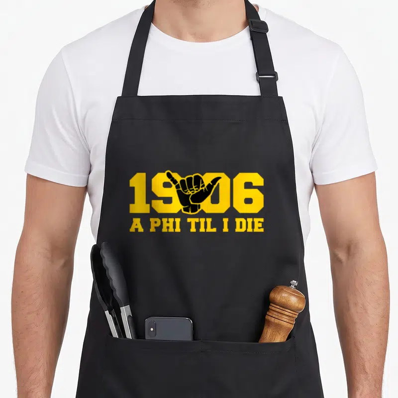 Fraternity african apron - Yellow 1906 text with black shaka hand and A PHI TIL I DIE slogan — shown on a black cotton canvas apron against a white background