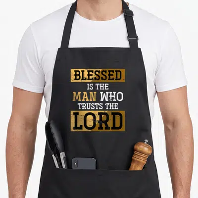 Christianity faith christian apron - Gold and white text reading BLESSED IS THE MAN WHO TRUSTS THE LORD on black — shown on a black cotton canvas apron against a white background