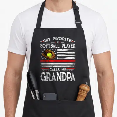 Call american flag apron - Softball glove neon ball bat flag distressed text My Favorite Softball Player Calls Me — shown on a black cotton canvas apron against a white background