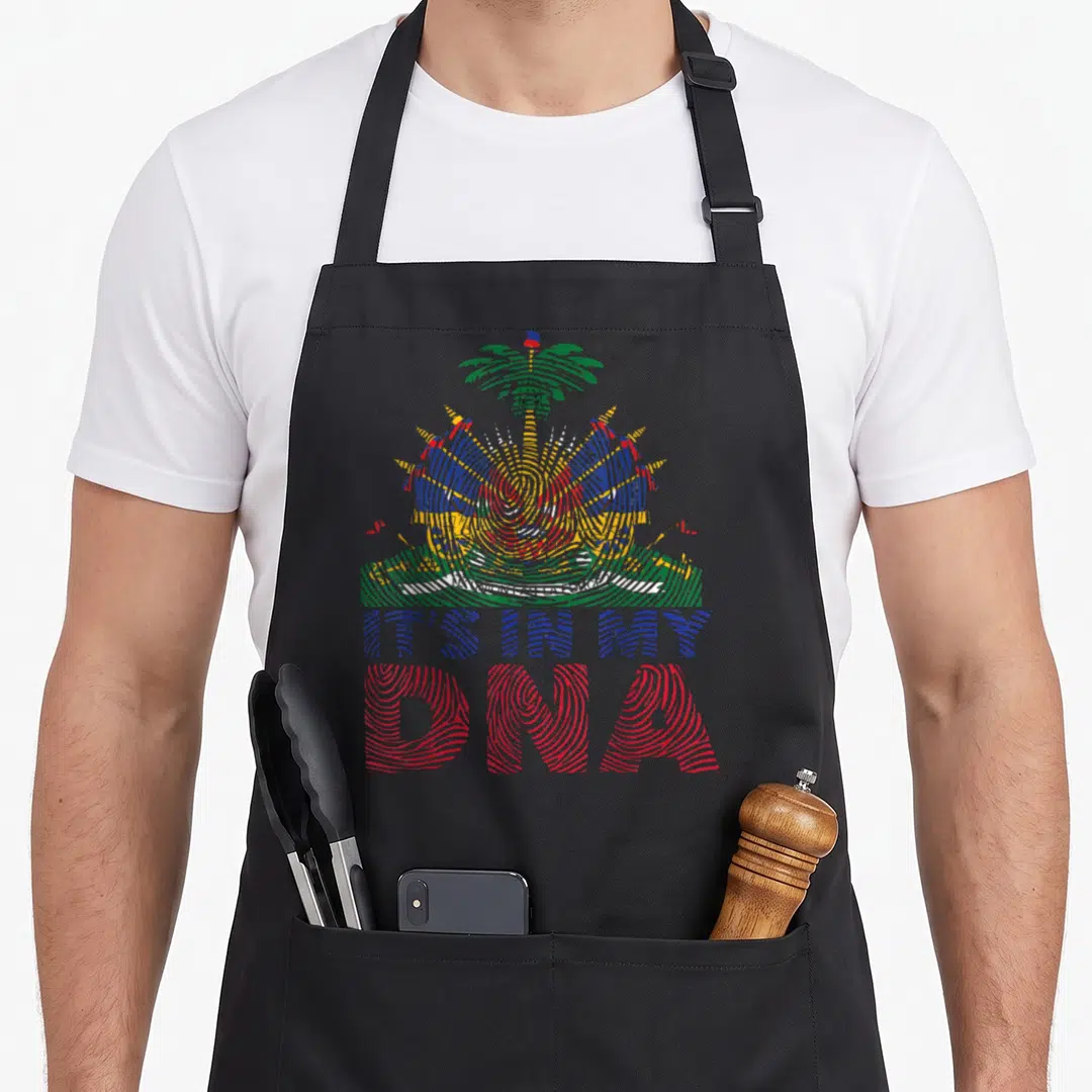 Flag creole lover apron - Distressed coat of arms in blue red yellow green above IT'S IN MY DNA text — shown on a black cotton canvas apron against a white background