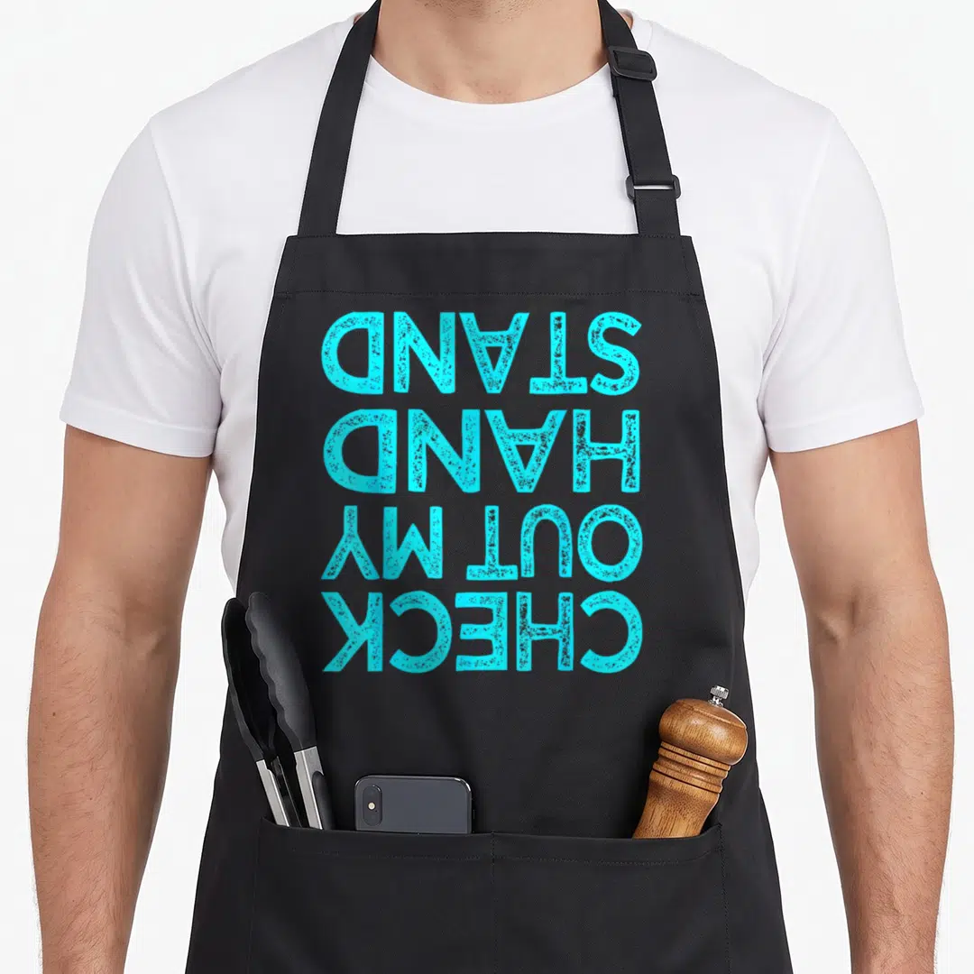 Check gymnastics apron - Inverted cyan text reading CHECK OUT MY HAND STAND stacked vertically — shown on a black cotton canvas apron against a white background