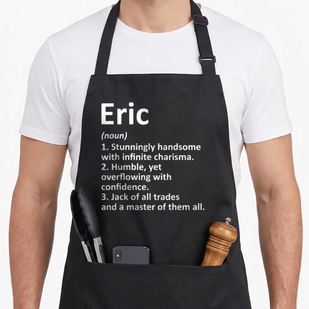 Eric father day aprons - White typography defining Eric as handsome and a master of all trades on grey background — shown on a black cotton canvas apron against a white background