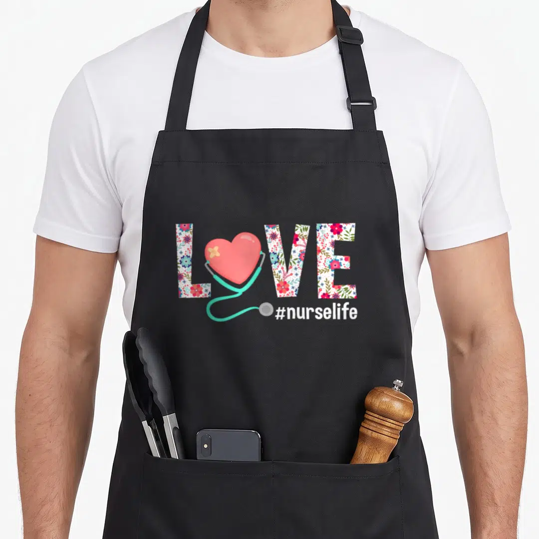 Nursing nurse apron - Floral LOVE text with bandaged heart, teal stethoscope, and #nurselife caption — shown on a black cotton canvas apron against a white background