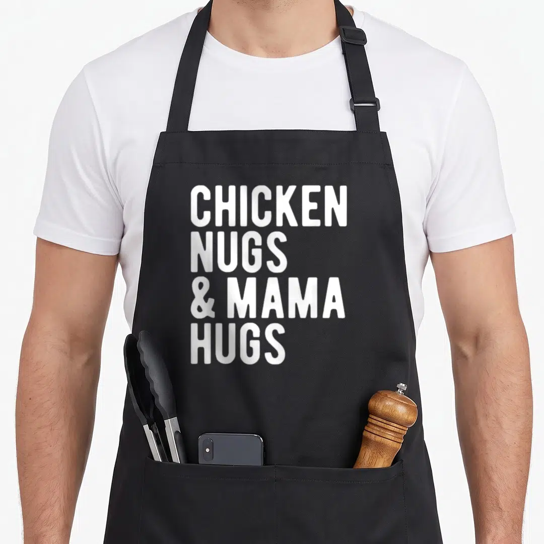 Mama hug chicken print apron - White stacked text reading CHICKEN NUGS & MAMA HUGS on black fabric — shown on a black cotton canvas apron against a white background