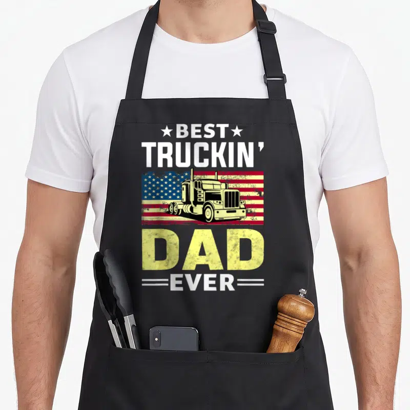 Trucking driver truck apron - Semi-truck on distressed flag with BEST TRUCKIN DAD EVER text and stars — shown on a black cotton canvas apron against a white background