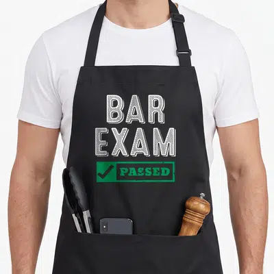 Bar lawyer apron - White BAR EXAM text above green rectangle with checkmark and PASSED — shown on a black cotton canvas apron against a white background