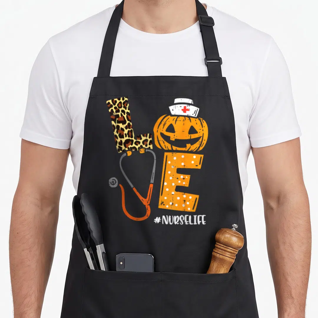 Leopard halloween nurse apron - LOVE formed by leopard L, pumpkin O with nurse hat, polka dot E, stethoscope V — shown on a black cotton canvas apron against a white background