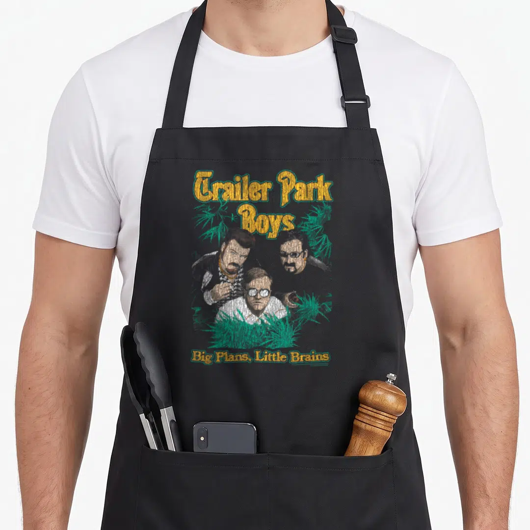 Funny park trailer apron - Arched yellow text above three cartoon men and green plants with bottom slogan on black — shown on a black cotton canvas apron against a white background