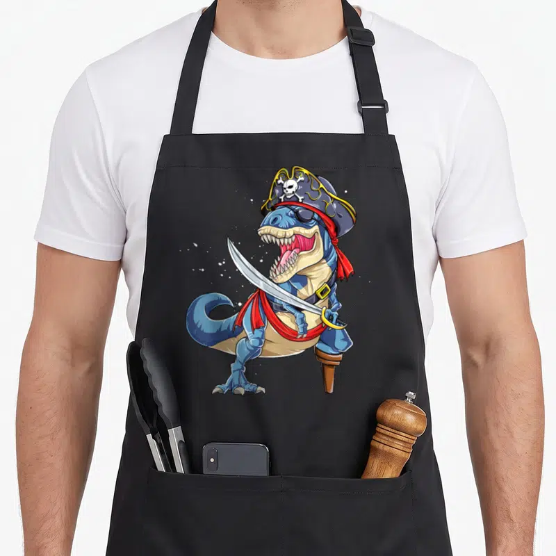 Jolly halloween apron - Blue cartoon dinosaur pirate wearing hat and eye patch holding a cutlass with a wooden peg leg — shown on a black cotton canvas apron against a white background