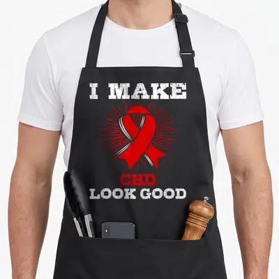 Funny chd congenital heart defect apron - Red awareness ribbon with sunburst and distressed I Make CHD Look Good text — shown on a black cotton canvas apron against a white background