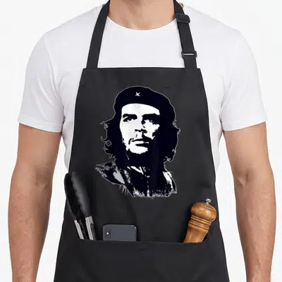 Che guanciale apron - Distressed black and white portrait of Che Guevara wearing a beret with a small star — shown on a black cotton canvas apron against a white background
