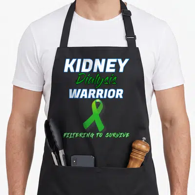 Kidney patient apron - Stacked KIDNEY Dialysis WARRIOR text with green awareness ribbon and filtering to survive slogan — shown on a black cotton canvas apron against a white background