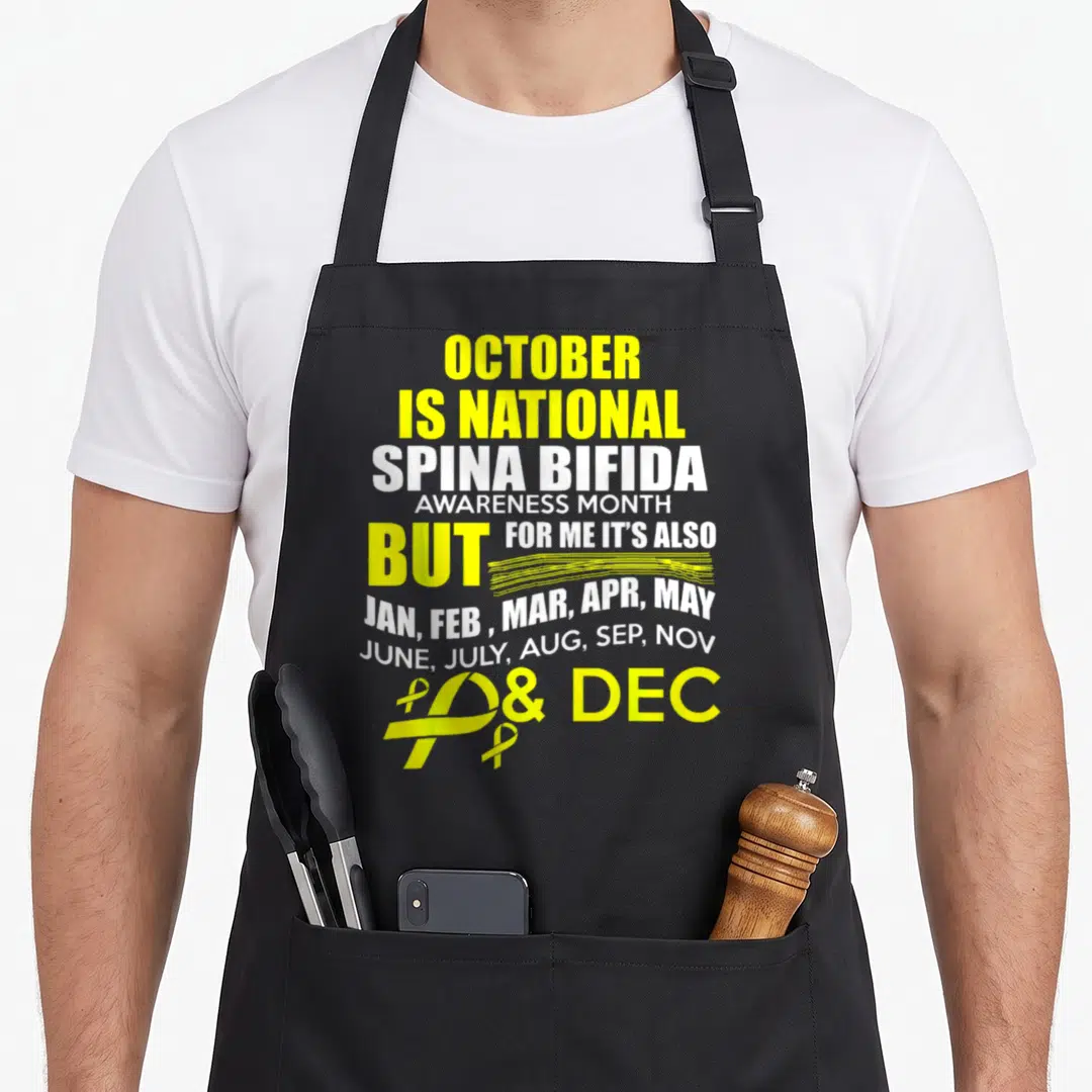 Support spina bifida awareness apron - Yellow and white text listing all months with two awareness ribbons at bottom — shown on a black cotton canvas apron against a white background
