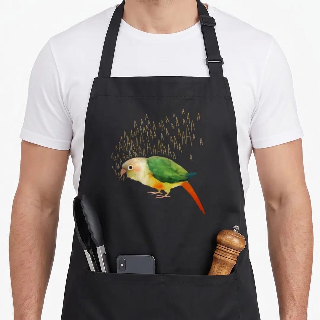 Screaming pineapple apron - Watercolor green bird with scattered gold A letters floating above its head — shown on a black cotton canvas apron against a white background