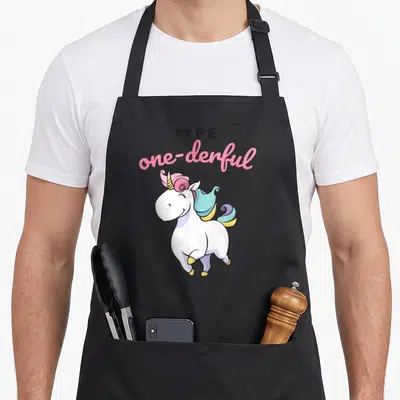 Onederful unicorn apron - Cartoon unicorn with pink mane and text TYPE one-derful — shown on a black cotton canvas apron against a white background