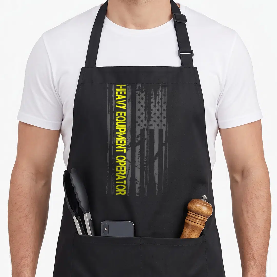Machinery heavy canvas aprons - Vertical yellow HEAVY EQUIPMENT OPERATOR text beside a distressed grey USA flag pattern — shown on a black cotton canvas apron against a white background