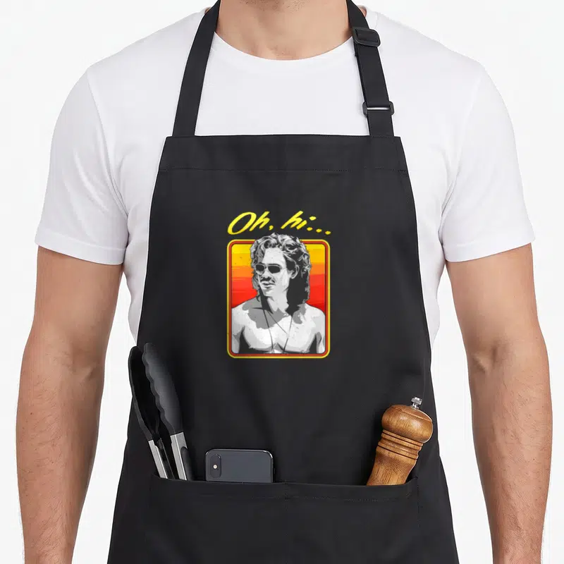 Boxed billy apron - Oh hi text above framed man portrait with yellow red grey white sunset background — shown on a black cotton canvas apron against a white background
