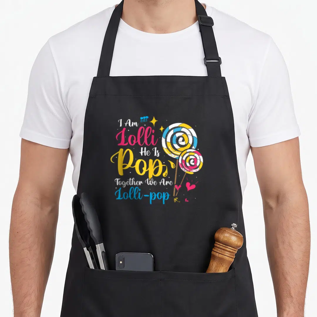 Pop grandmother apron - I Am Lolli He Is Pop text with two swirl lollipops and hearts — shown on a black cotton canvas apron against a white background