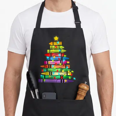 Crayon christmas tree apron - Stacked yellow green red blue purple crayons forming a tree with a star and lights — shown on a black cotton canvas apron against a white background
