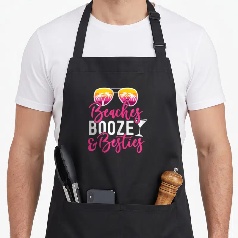 Weekend friends apron - Sunglasses with palm tree reflection and stacked text reading Beaches BOOZEY Besties — shown on a black cotton canvas apron against a white background
