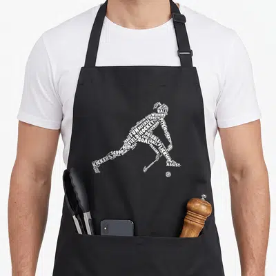 Player field apron - White word art silhouette of a hockey player formed by text like BALL, GOAL, and STICK — shown on a black cotton canvas apron against a white background