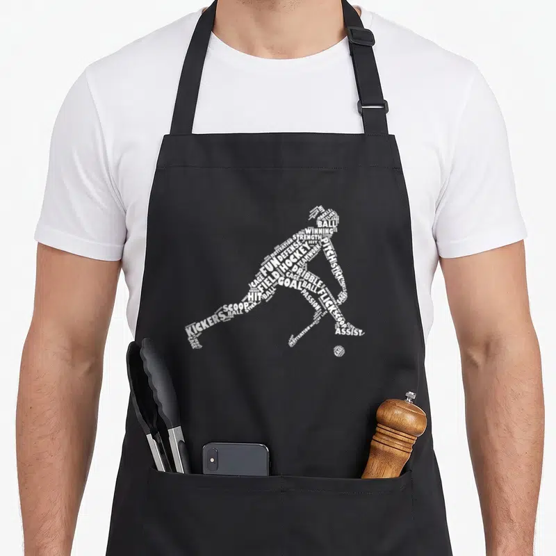 Player field apron - White word art silhouette of a hockey player formed by text like BALL, GOAL, and STICK — shown on a black cotton canvas apron against a white background