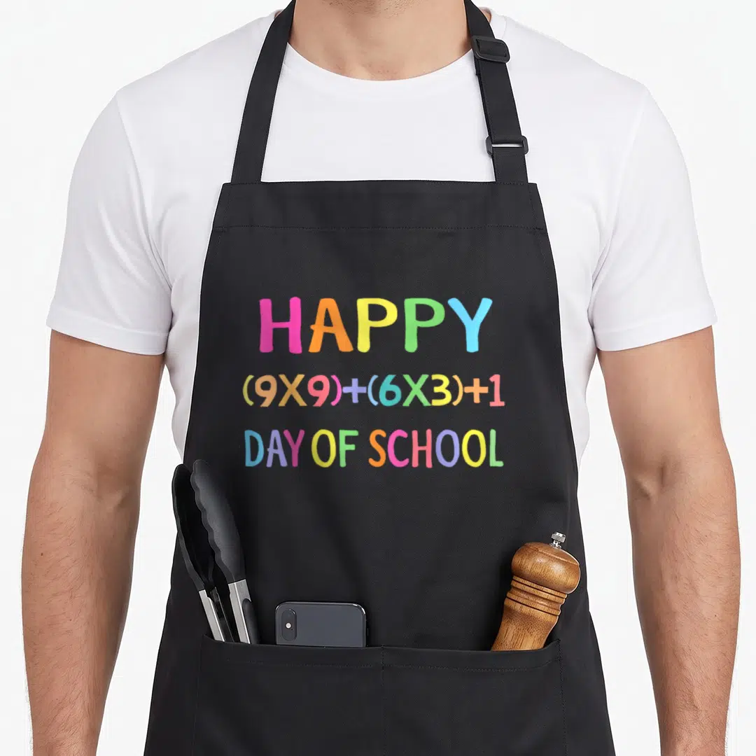 Formula teacher apron - Colorful text reading Happy 9x9 plus 6x3 plus 1 Day of School — shown on a black cotton canvas apron against a white background