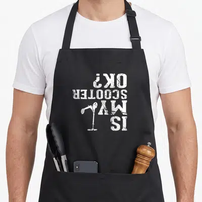 Funny stunt scooter apron - Upside down white text IS MY SCOOTER OK with scooter graphic distressed style — shown on a black cotton canvas apron against a white background