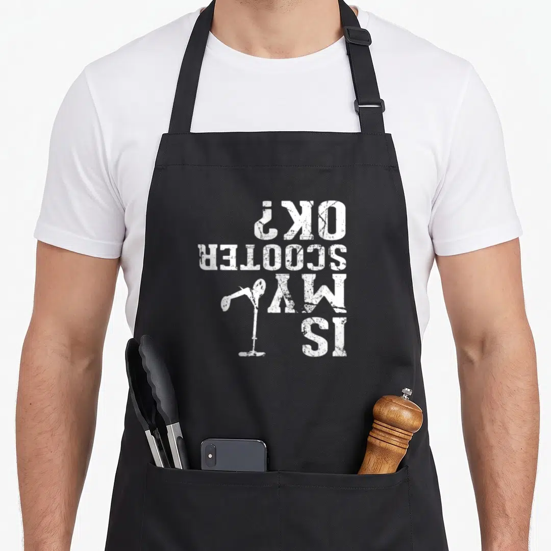 Funny stunt scooter apron - Upside down white text IS MY SCOOTER OK with scooter graphic distressed style — shown on a black cotton canvas apron against a white background