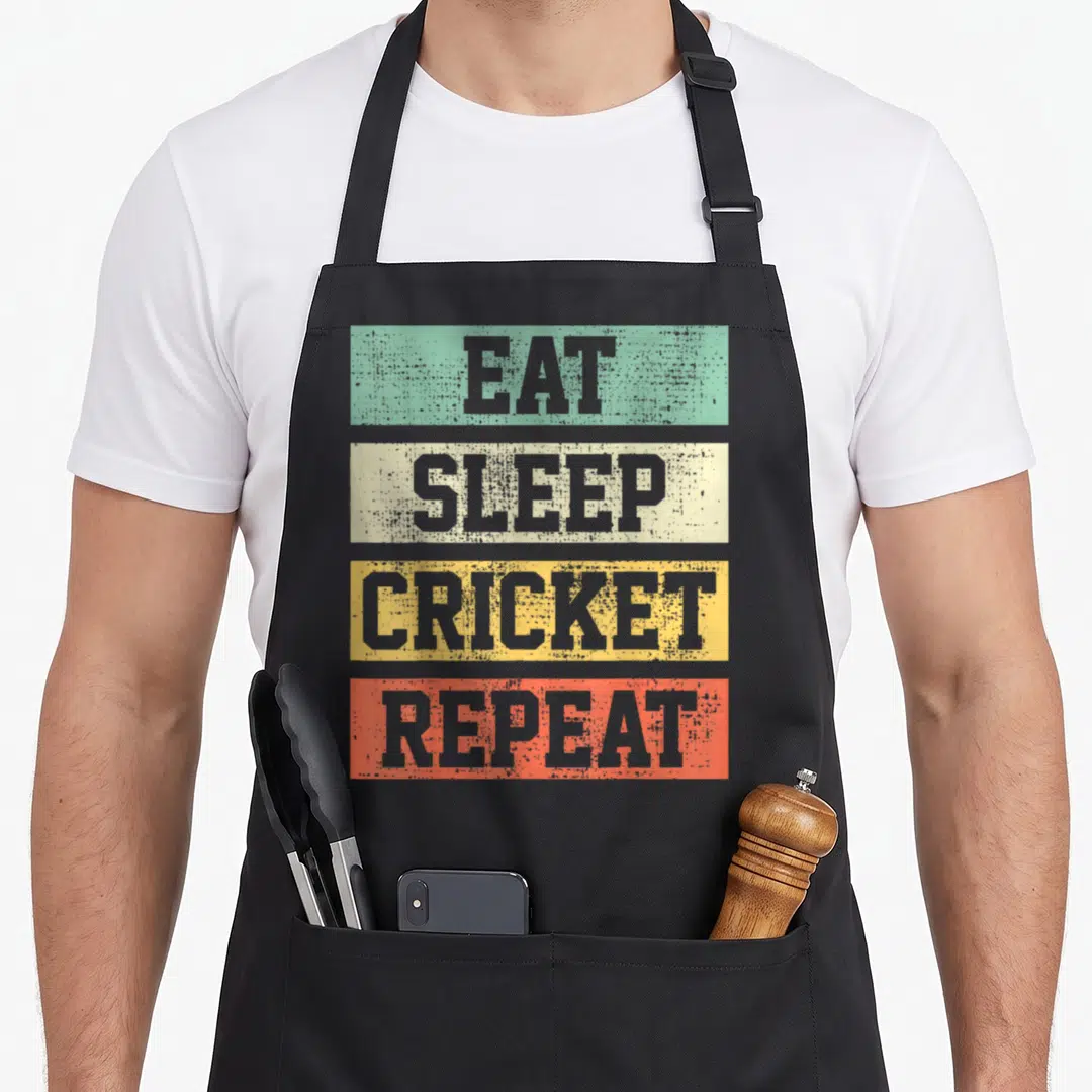 Coach cricket apron - Stacked text EAT SLEEP CRICKET REPEAT on green beige yellow and red bars — shown on a black cotton canvas apron against a white background