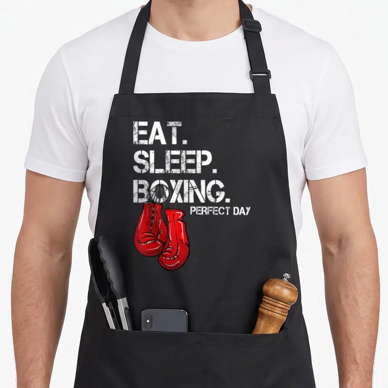 Eat boxing apron - Red boxing gloves hanging from white distressed text EAT SLEEP BOXING PERFECT DAY — shown on a black cotton canvas apron against a white background
