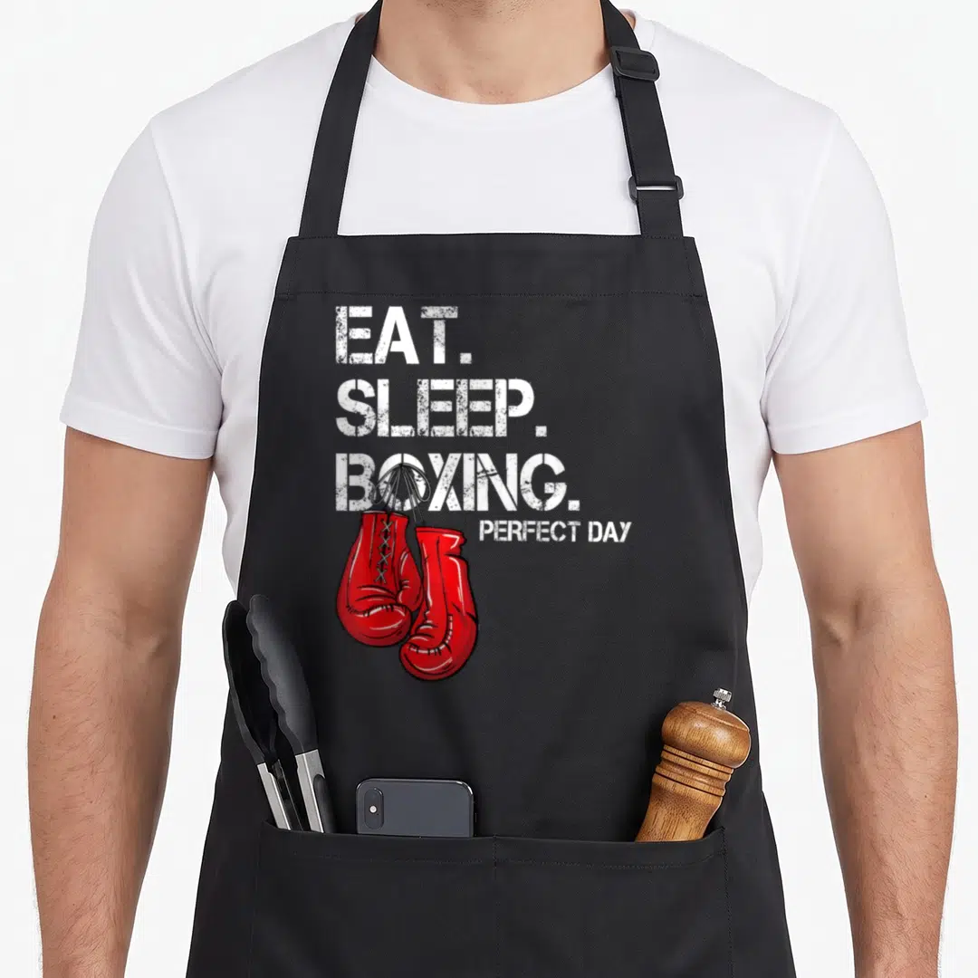 Eat boxing apron - Red boxing gloves hanging from white distressed text EAT SLEEP BOXING PERFECT DAY — shown on a black cotton canvas apron against a white background