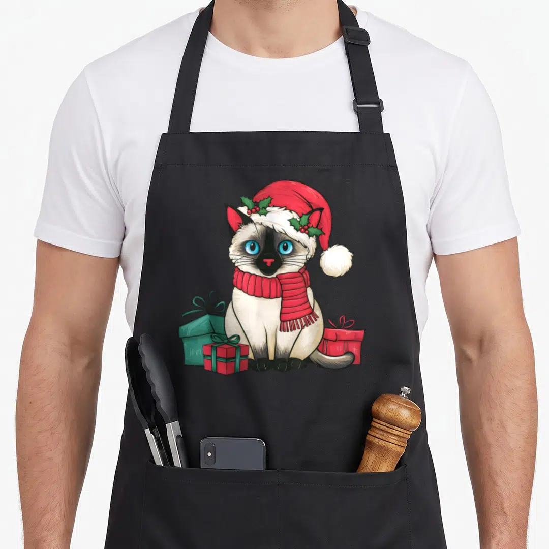 Xmas cute cat aprons - Cartoon Siamese cat in red Santa hat and scarf sitting among red and teal gift boxes — shown on a black cotton canvas apron against a white background