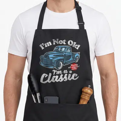 Pickup birthday truck apron - Blue classic truck illustration with I'm Not Old text and red starburst badge — shown on a black cotton canvas apron against a white background