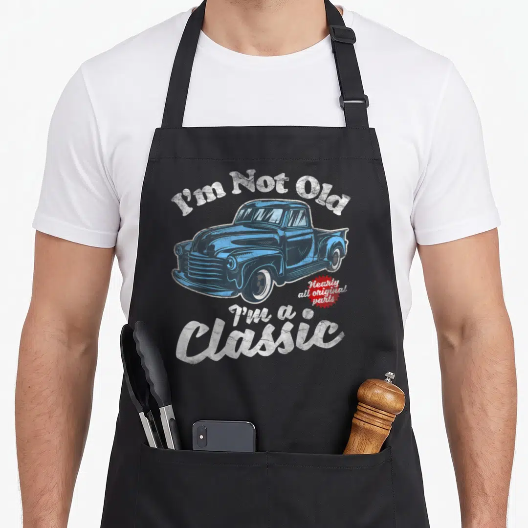 Pickup birthday truck apron - Blue classic truck illustration with I'm Not Old text and red starburst badge — shown on a black cotton canvas apron against a white background