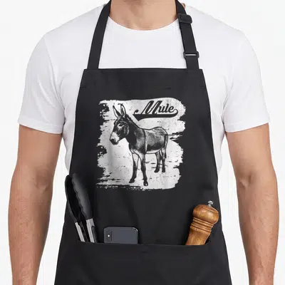 Mug mule apron - Grey mule illustration on distressed white paint splash background with retro Mule text — shown on a black cotton canvas apron against a white background