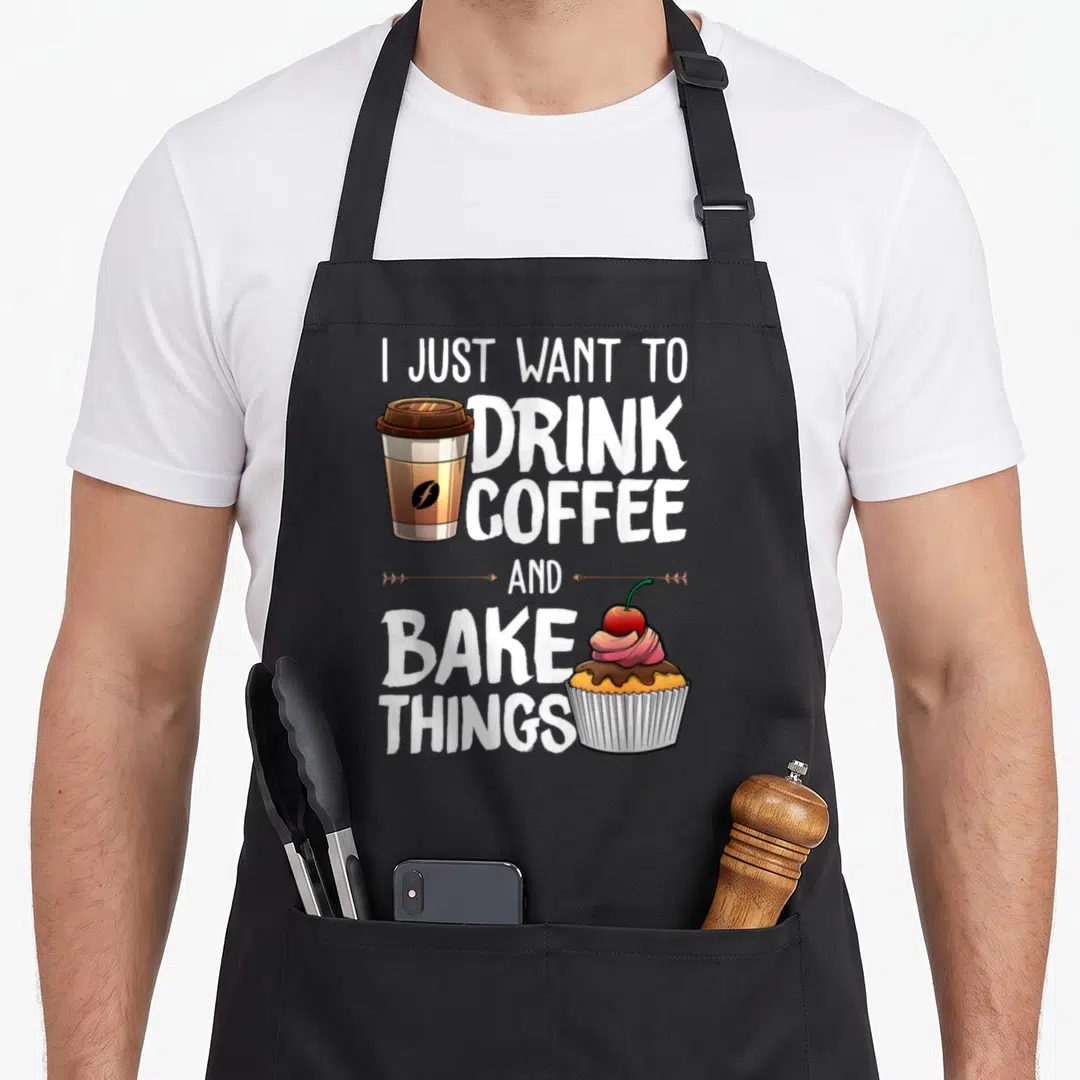Drinking baker apron - Stacked text reading I Just Want to Drink Coffee and Bake Things with a coffee cup and cupcake — shown on a black cotton canvas apron against a white background