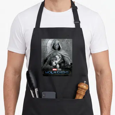 Glowing moon apron - Moon Knight poster art with hooded figure and hieroglyphics on black apron — shown on a black cotton canvas apron against a white background