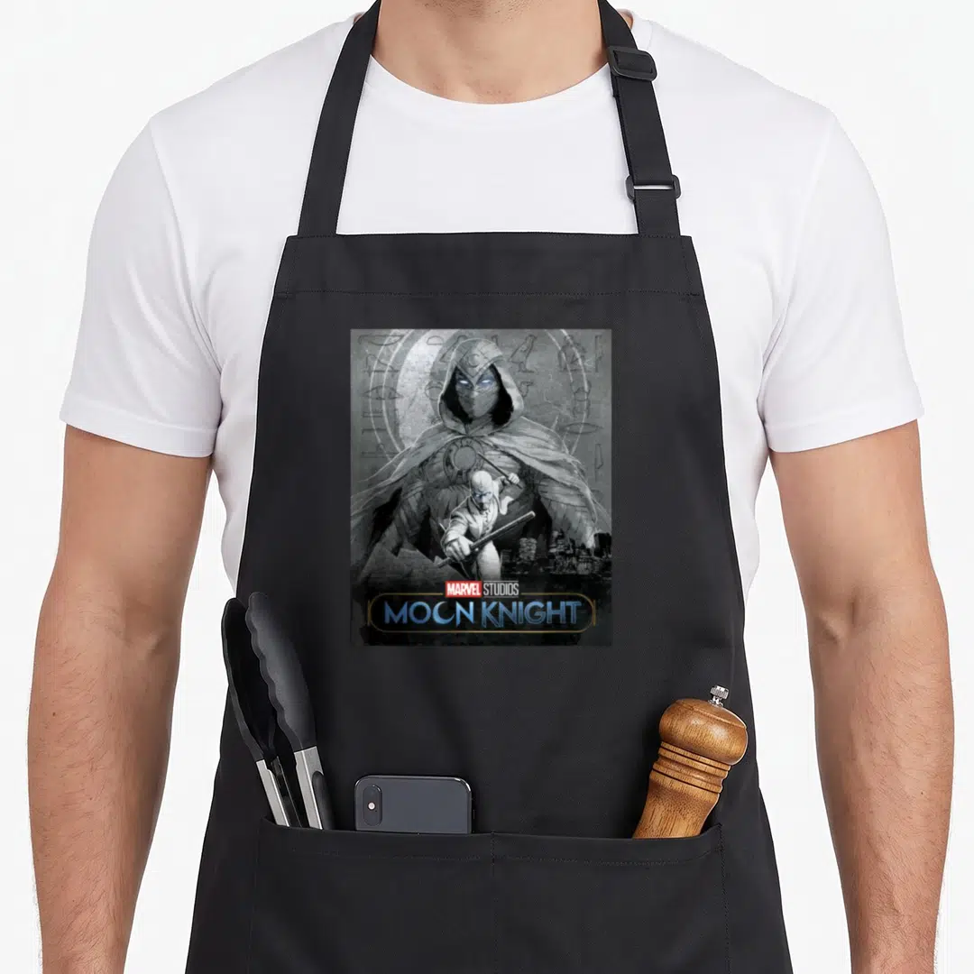 Glowing moon apron - Moon Knight poster art with hooded figure and hieroglyphics on black apron — shown on a black cotton canvas apron against a white background