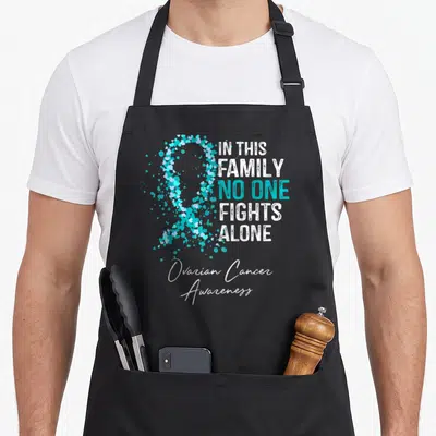 Ovarian family aprons - Teal heart ribbon with stacked text IN THIS FAMILY NO ONE FIGHTS ALONE and Ovarian Cancer — shown on a black cotton canvas apron against a white background