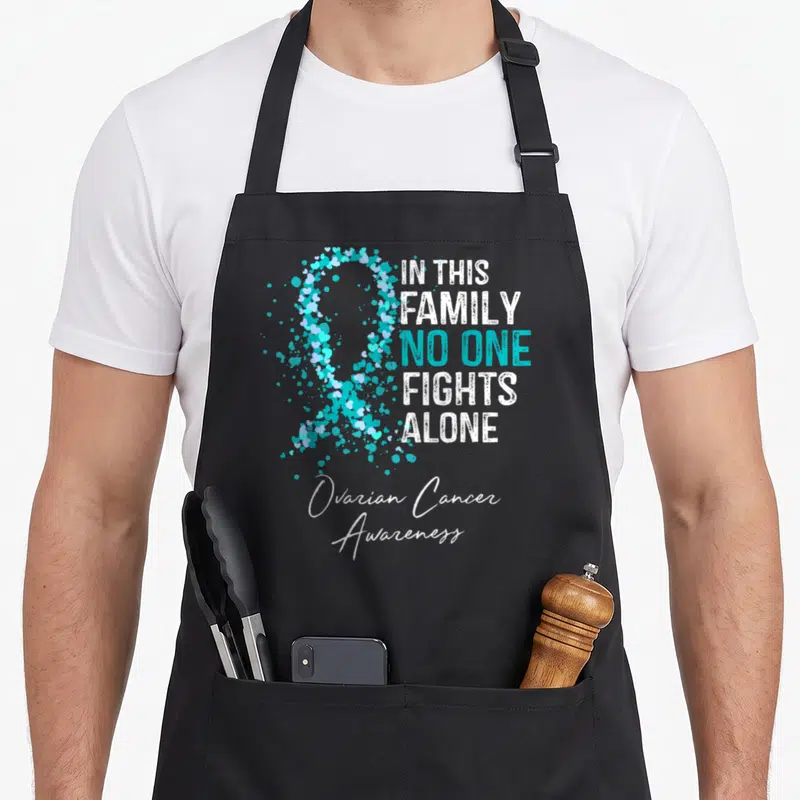 Ovarian family aprons - Teal heart ribbon with stacked text IN THIS FAMILY NO ONE FIGHTS ALONE and Ovarian Cancer — shown on a black cotton canvas apron against a white background