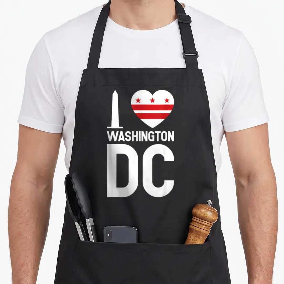 Funny washington pride apron - White Washington Monument next to red-striped heart with WASHINGTON DC text below — shown on a black cotton canvas apron against a white background