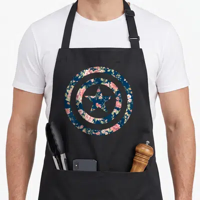 Icon floral apron - Circular shield and star filled with pink, green, and dark blue floral pattern — shown on a black cotton canvas apron against a white background