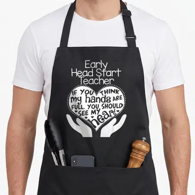 Early start teacher apron - White heart held by hands with text Early Head Start Teacher and inspirational quote — shown on a black cotton canvas apron against a white background